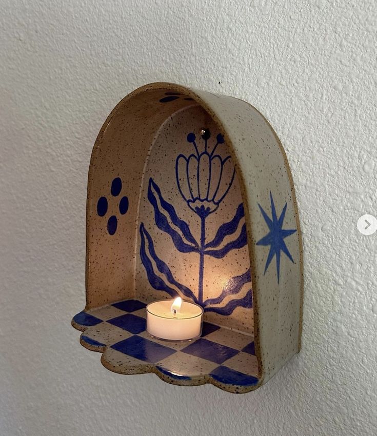 a candle holder with a blue and white design on the wall next to a lit candle