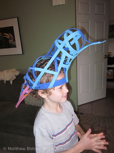 a young boy wearing a paper hat made to look like a bird with blue strips on it