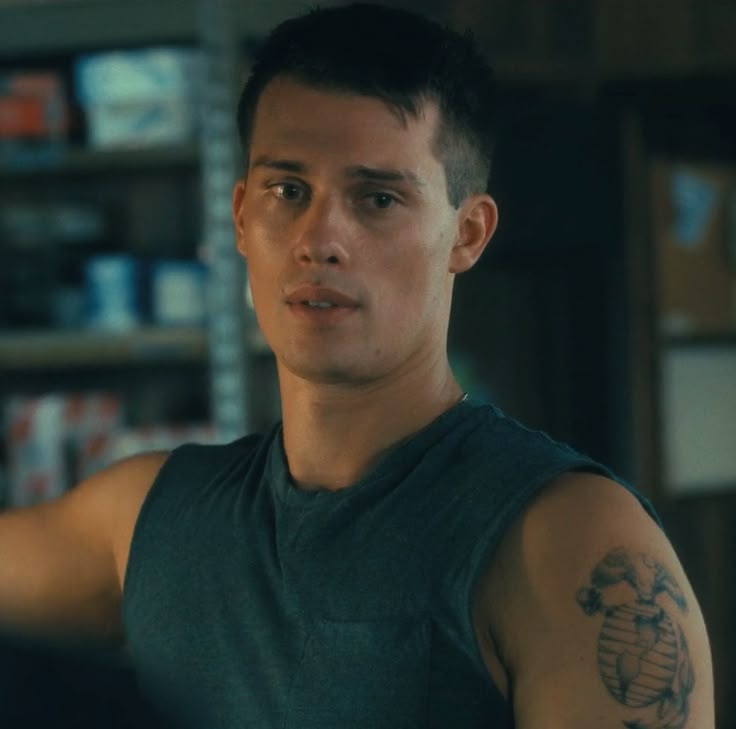 a man with a tattoo on his arm standing in front of a bookshelf