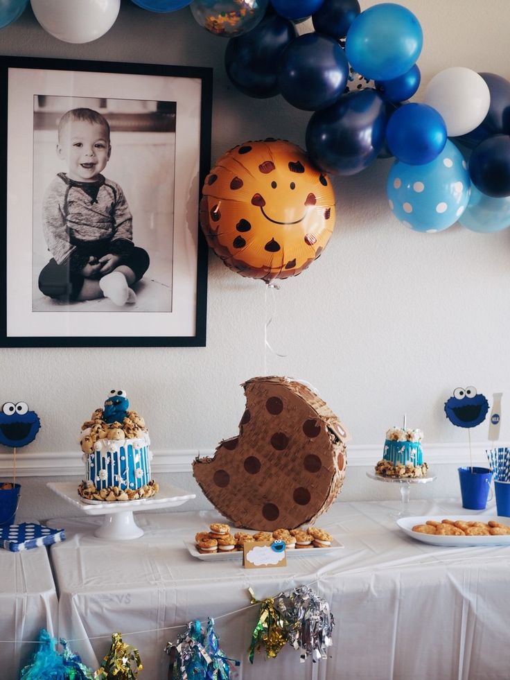 a table topped with lots of desserts and balloons in front of a wall filled with pictures