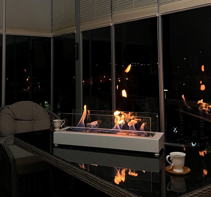 a fire pit sitting on top of a glass table in front of a large window