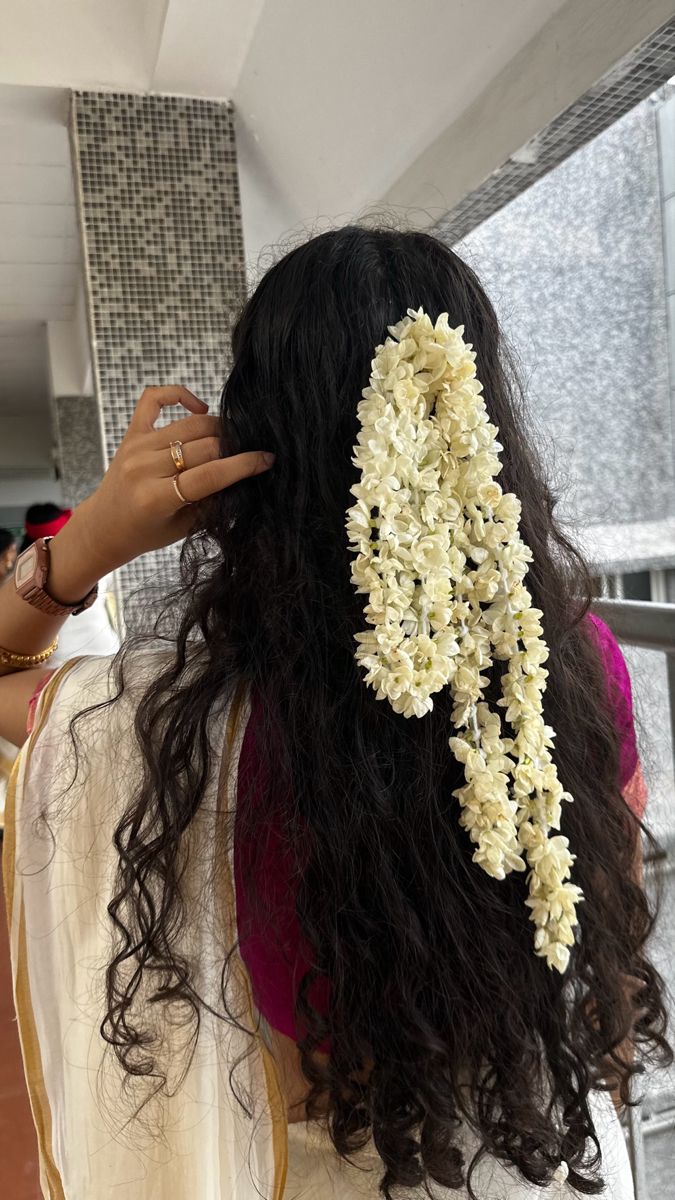 a woman with long black hair is holding flowers in her hair