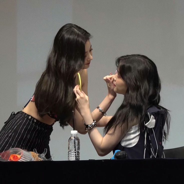 two young women standing next to each other at a table with a banana in their mouth