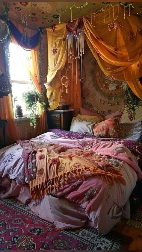 a bed covered in lots of blankets and pillows next to a window with curtains on it