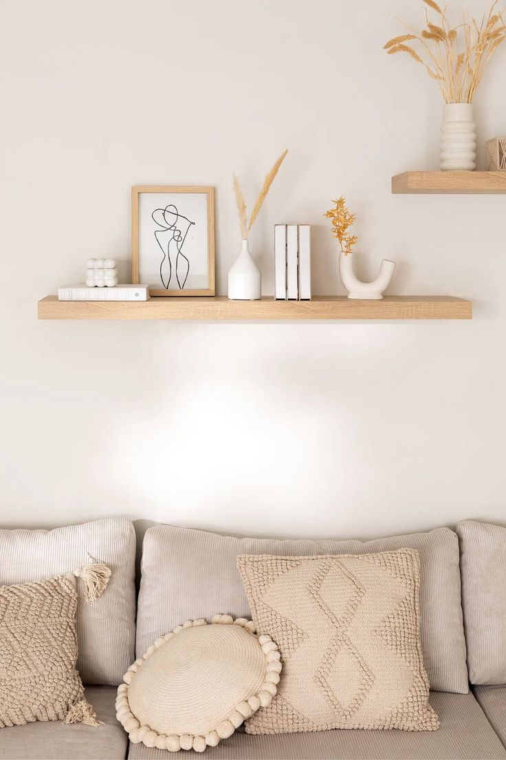 a couch with some pillows on top of it next to two bookshelves and vases