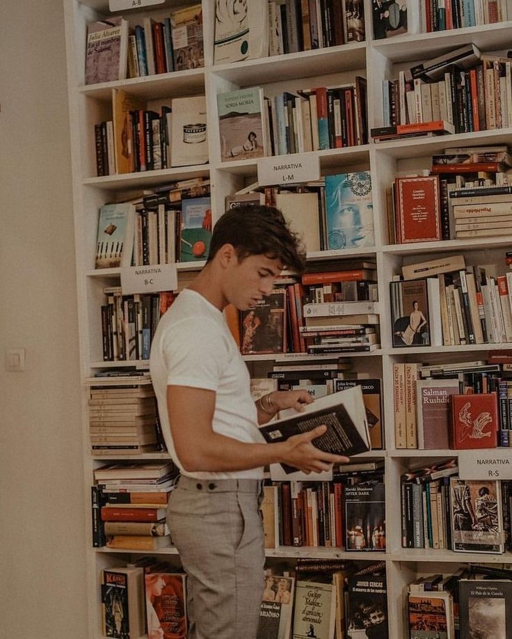 a man reading a book in front of a bookshelf full of books on it