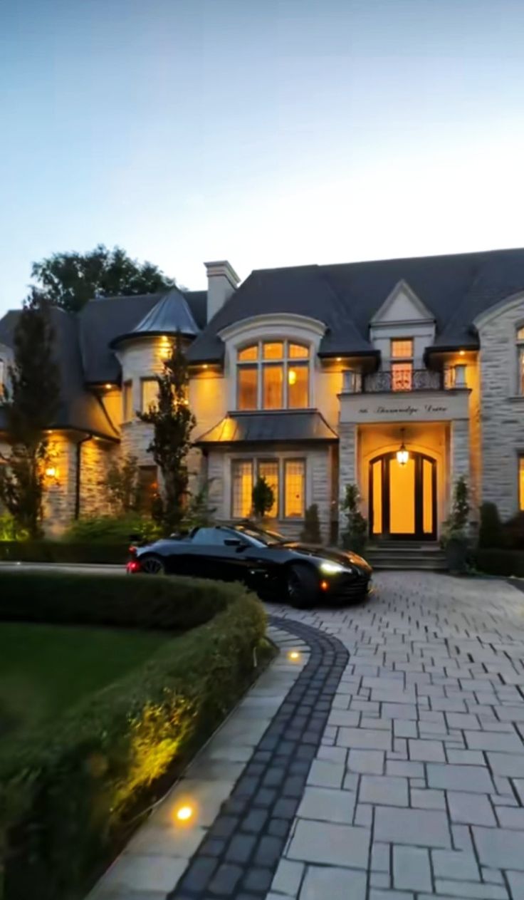 two cars are parked in front of a large house at night with the lights on