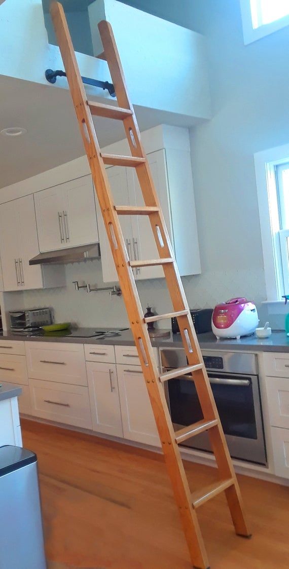 a ladder is in the middle of a kitchen with white cabinets and wood flooring