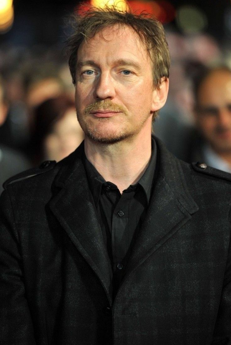 a man in a black suit looks off into the distance as he stands on a red carpet