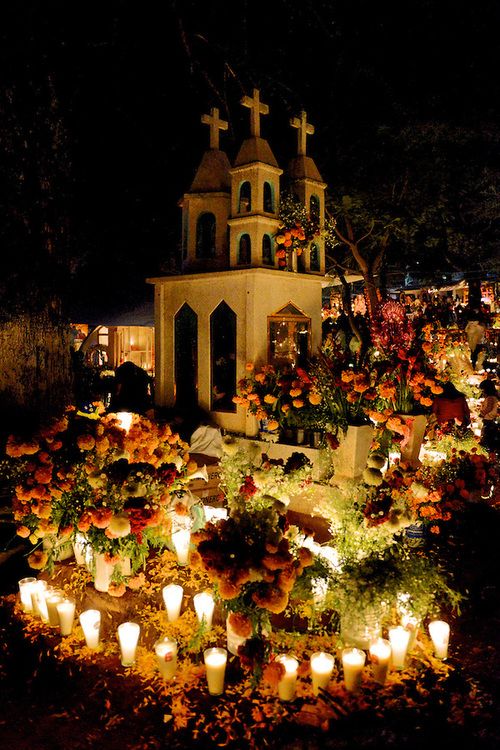 many candles are lit in front of a church with crosses and flowers on the ground