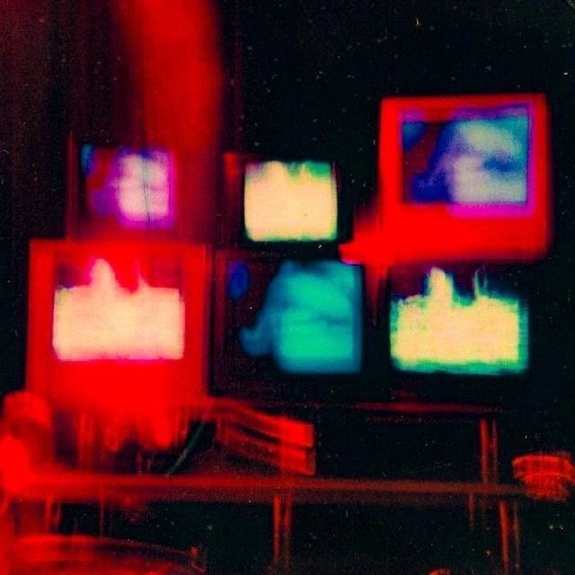 multiple televisions are shown with red and blue lights in the dark, one is blurry