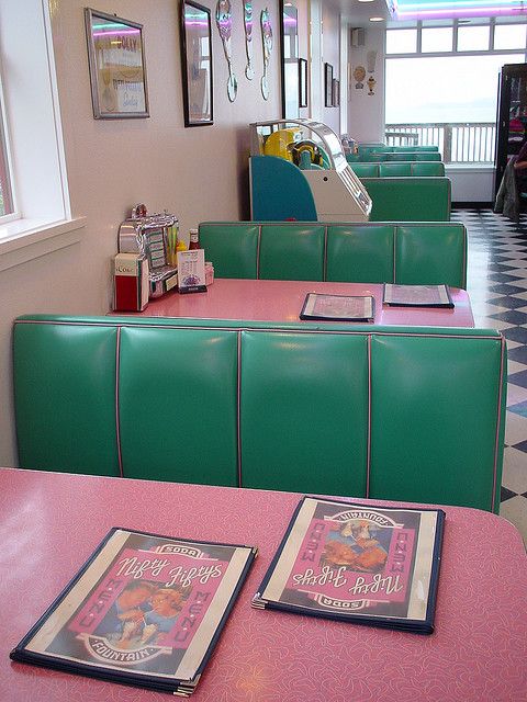 tables and booths in a restaurant with posters on the wall behind them that are green