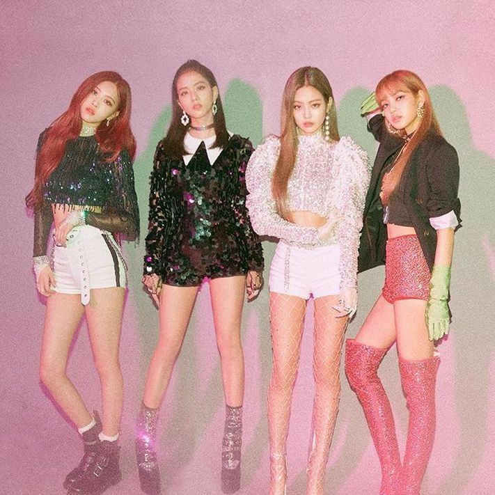 four girls standing in front of a pink background wearing short shorts and knee high boots