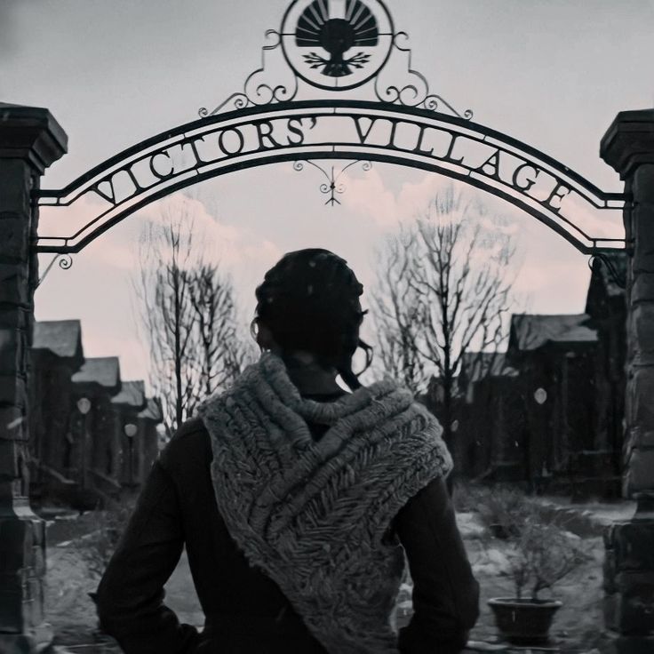 black and white photograph of a person wearing a scarf in front of a sign that says victoria's village