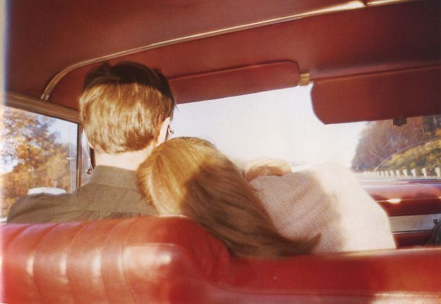 two people sitting in the back seat of a red car, looking out the window