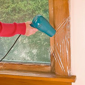 a woman blow drying her hair in front of a window with an electric dryer