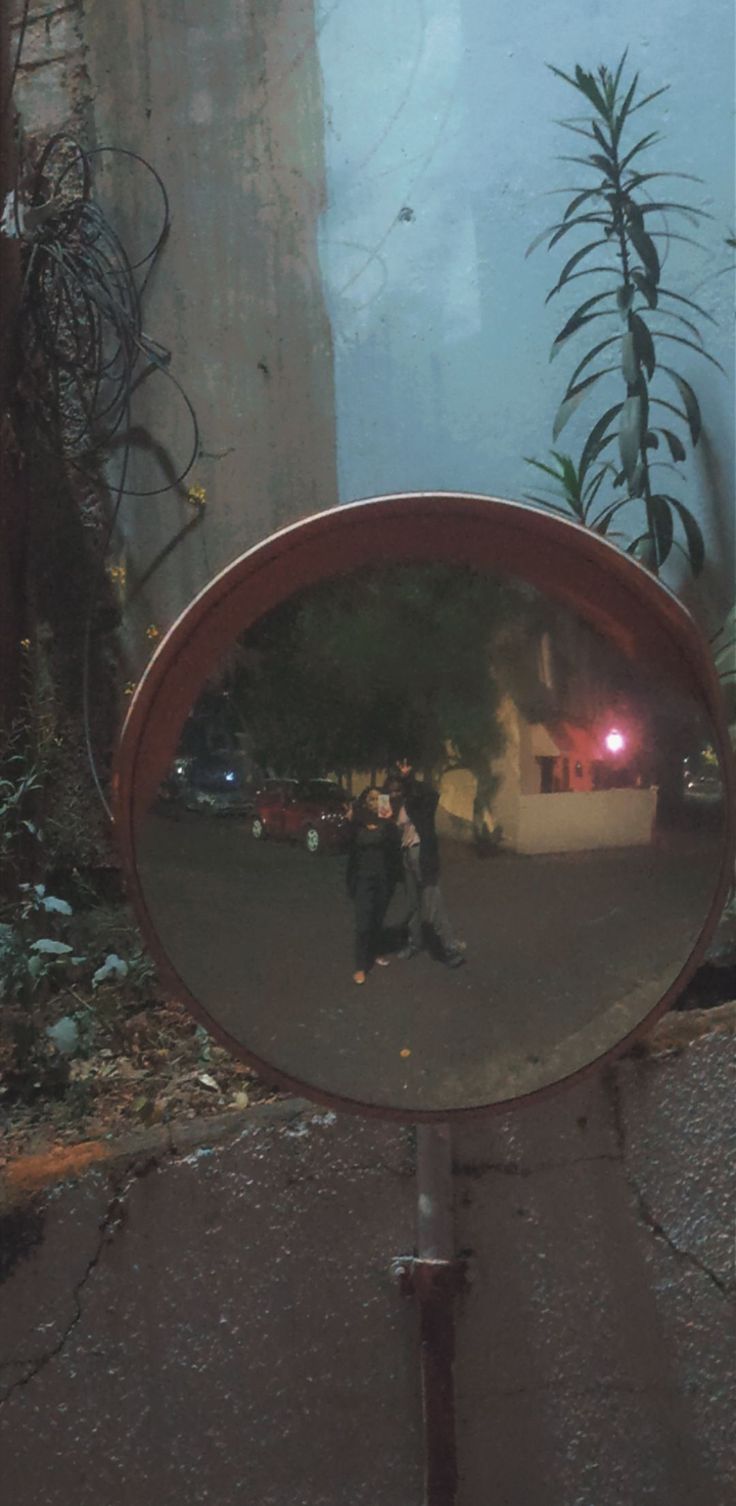 the reflection of two people in a round mirror on a metal pole near a building