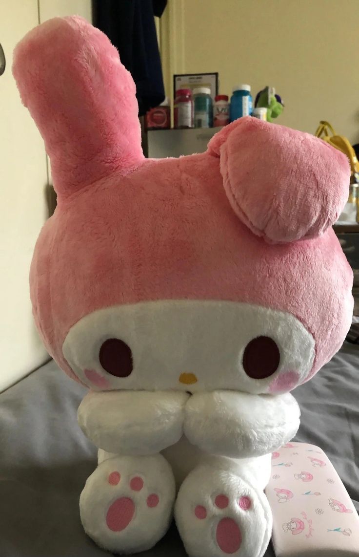 a pink hello kitty stuffed animal sitting on top of a bed next to a pillow