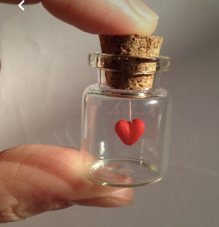 a hand holding a tiny glass bottle with a cork and red heart in the inside