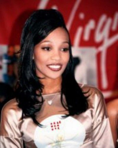 a woman with long black hair wearing a gold dress and smiling at the camera while standing in front of a coca cola sign