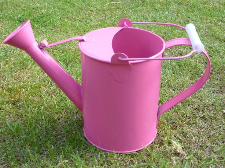 a pink watering can sitting in the grass