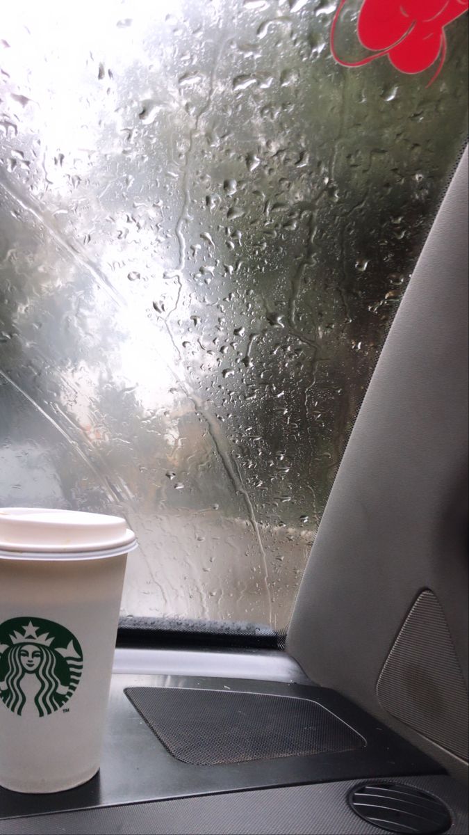 a starbucks cup sitting on top of a table next to a window covered in rain