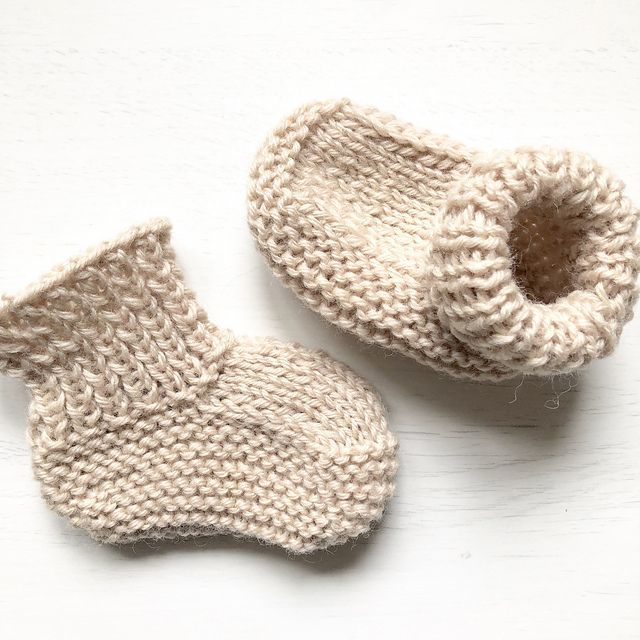 two knitted baby booties sitting next to each other on a white table top