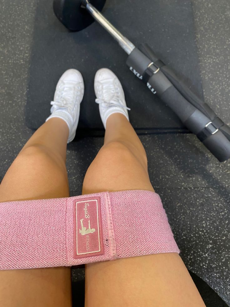 a woman's legs with a pink band around her ankles and a barbell in the background