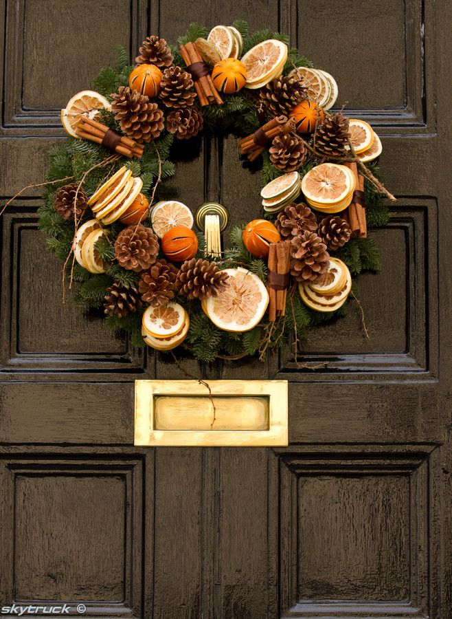 a wreath with oranges and pine cones hanging on the front door to decorate it