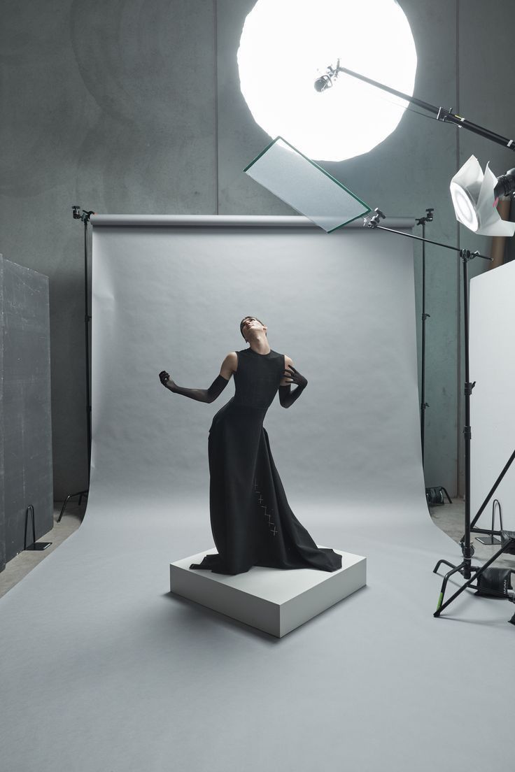 a woman in a black dress is standing on a white platform with her arms outstretched