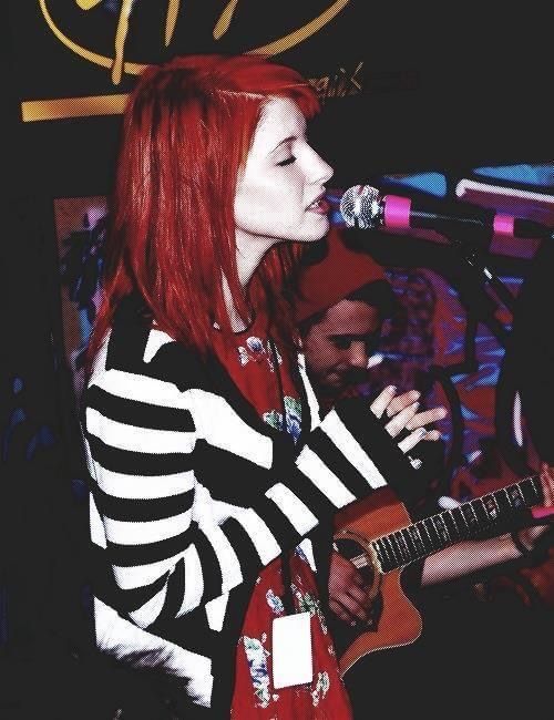 a woman with red hair is singing into a microphone and holding a guitar in front of her