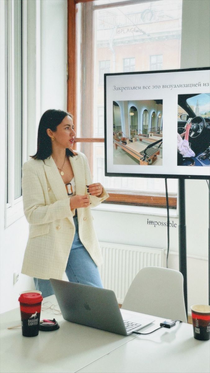 a woman standing in front of a laptop computer next to a screen with pictures on it