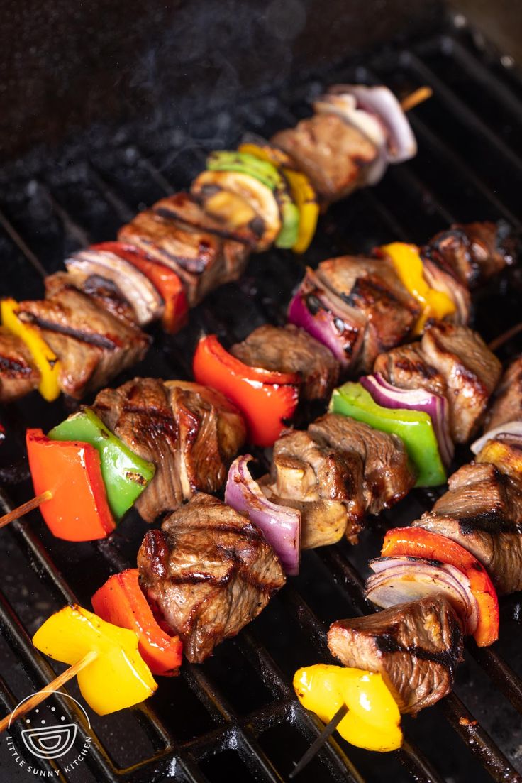 several skewers of meat and vegetables cooking on a grill