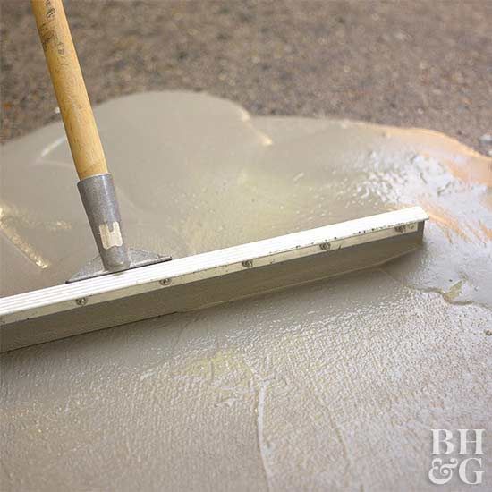 a close up of a person using a paint roller on cement with a brush in it