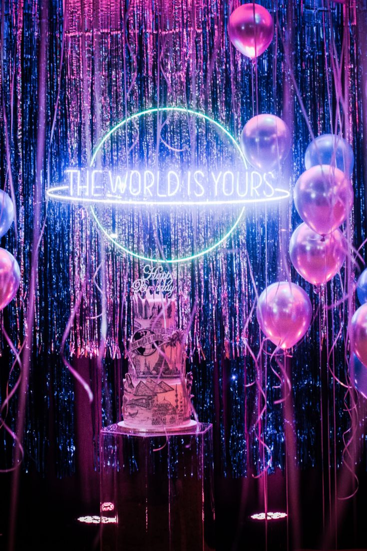 the world is yours sign on display in front of balloons and streamers with neon lights