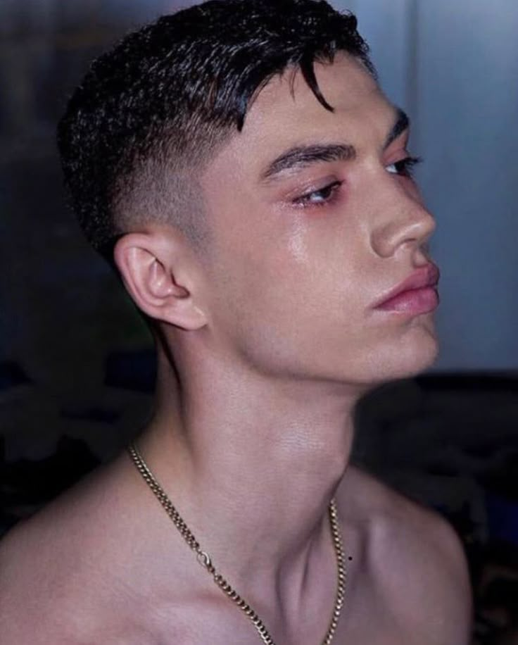 a shirtless young man wearing a chain around his neck looking off into the distance