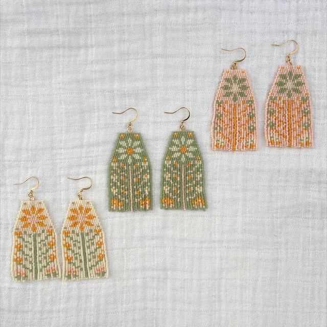 three pairs of beaded earrings on a white cloth background, each with an orange and green design