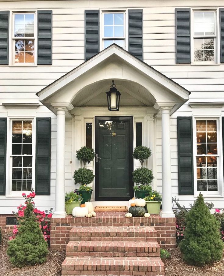 a black front door and steps leading up to a white house with green shutters