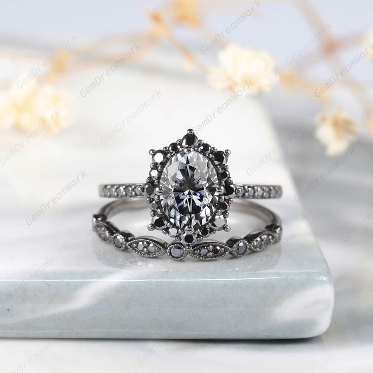 an oval cut engagement ring with black diamond accents on a white marble surface next to flowers