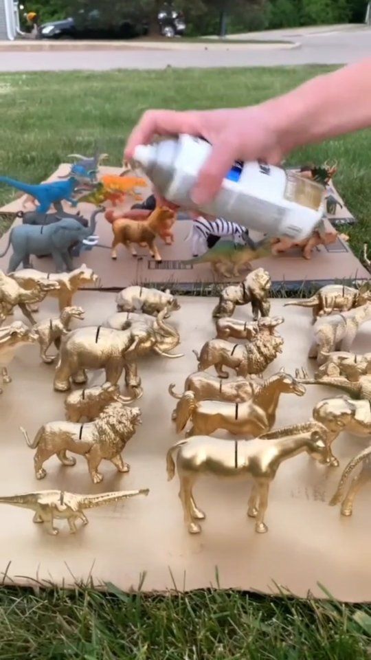 a person is spray painting gold toy animals on a sheet of paper in the grass