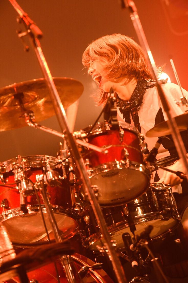 a man with long hair playing drums in front of a red stage light and microphone