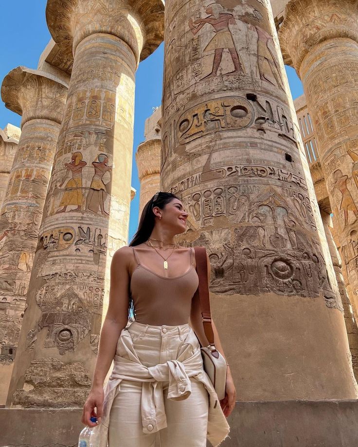 a woman standing in front of some very tall pillars with paintings on it's sides