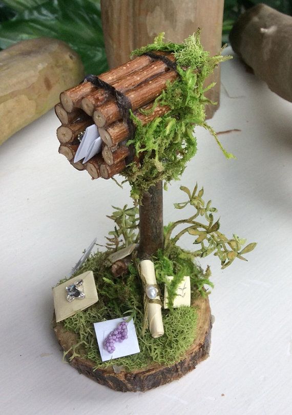 a miniature tree house made out of logs and moss with pictures on the top, sitting on a table