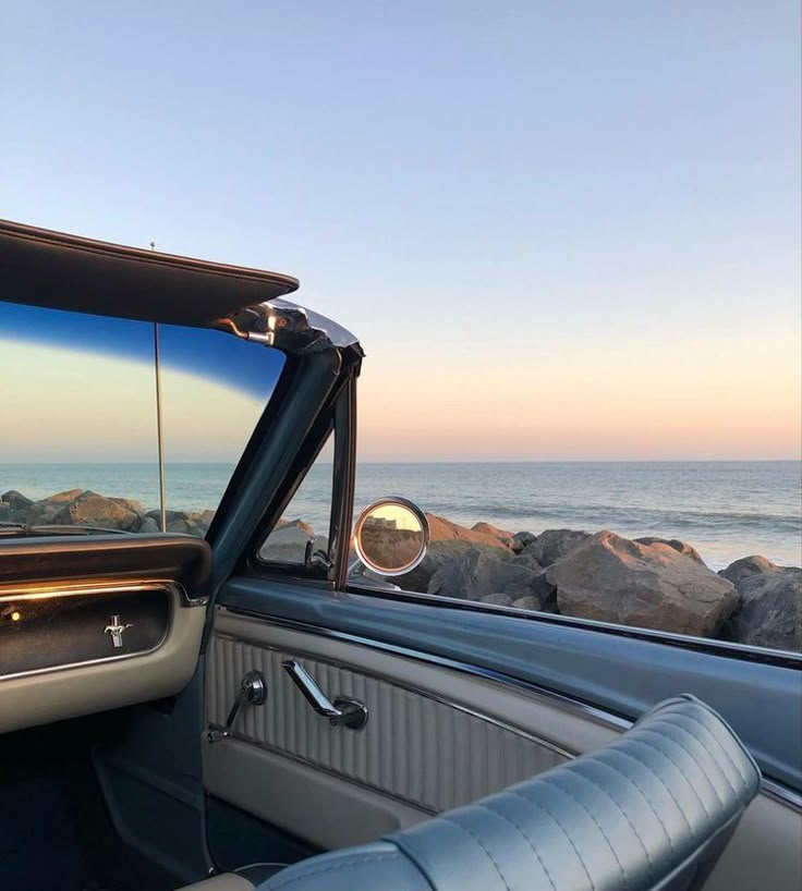 an open car door with the ocean in the back ground and rocks on the side