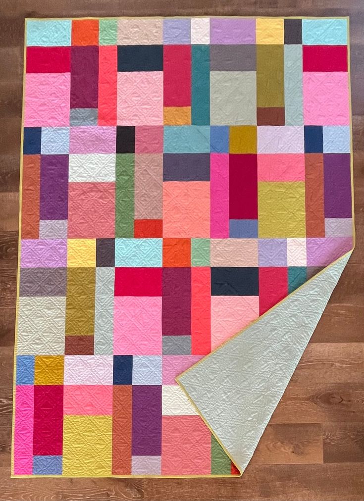 a multicolored patchwork quilt is laying on a wooden floor next to a folded piece of paper