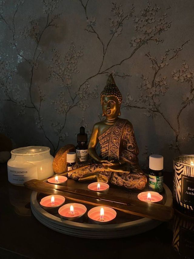 a buddha statue sitting on top of a wooden table next to candles and other items