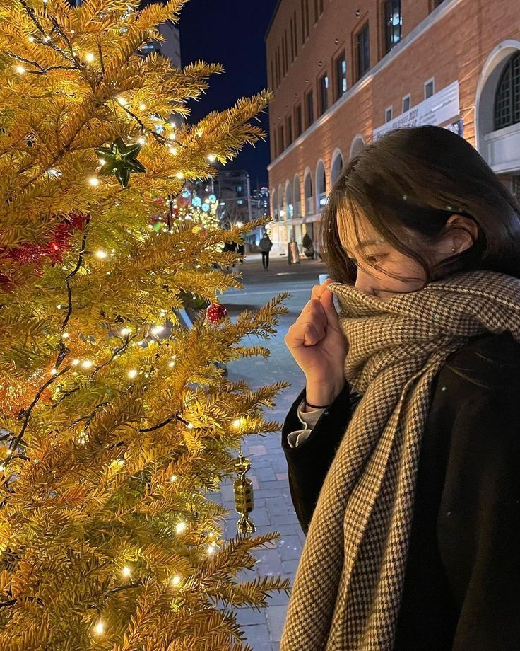 a woman standing in front of a christmas tree with lights on it's branches