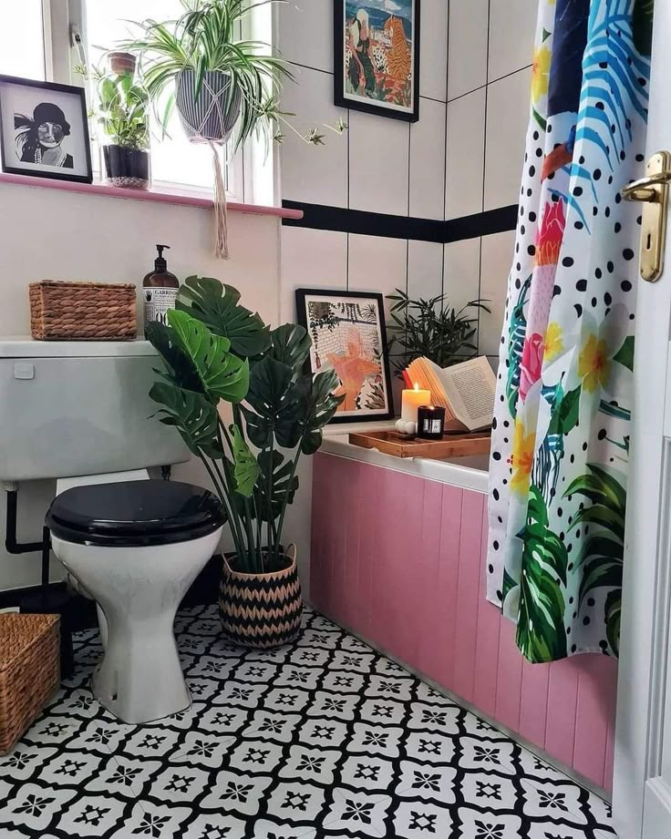 a bathroom with potted plants and pictures on the wall above the toilet, along with a black and white patterned rug