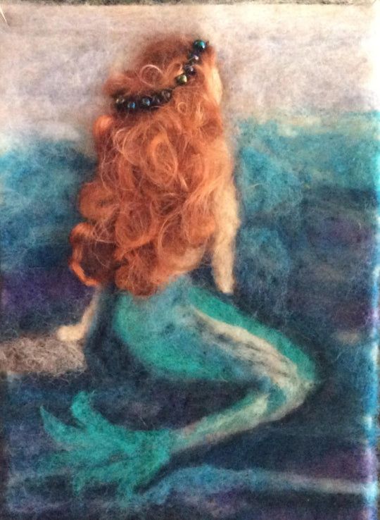 a needle - felted mermaid sitting on the ocean floor with her tail curled up