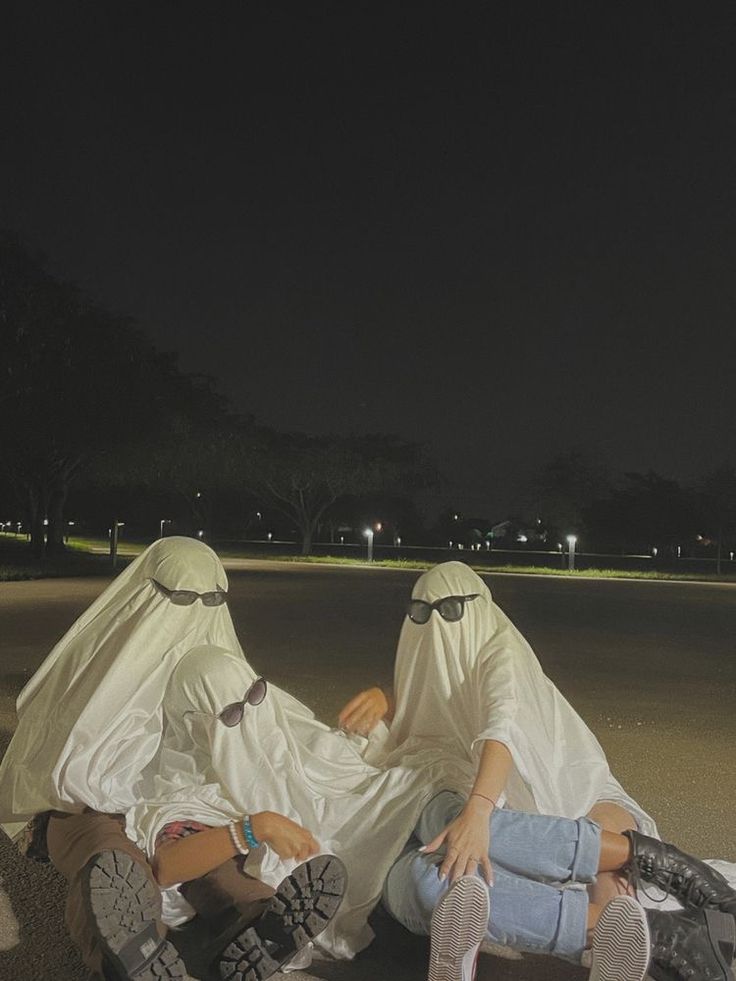 two people sitting on the ground with their heads covered by white cloths at night